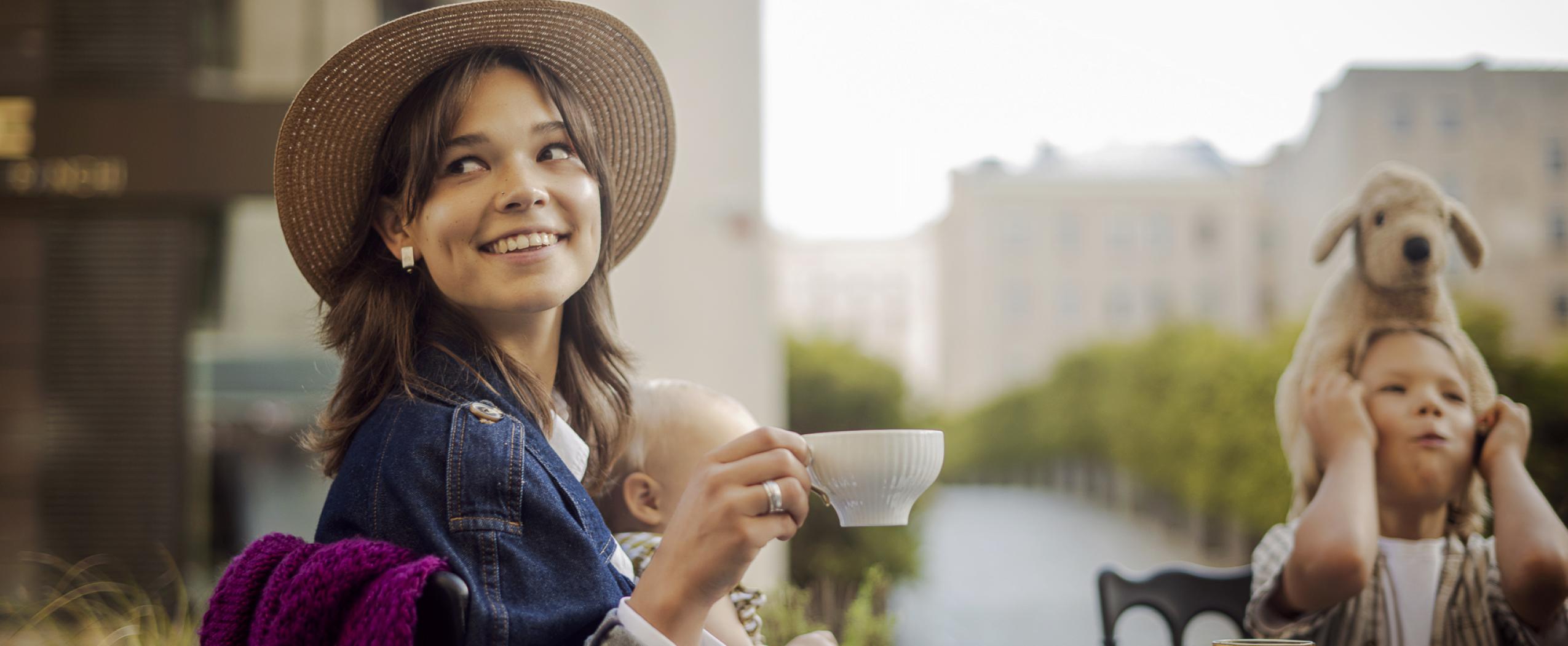 A young woman with two small children enjoys time at a café with the CENTRUS quarter visible in the background on Dzirnavu Street.