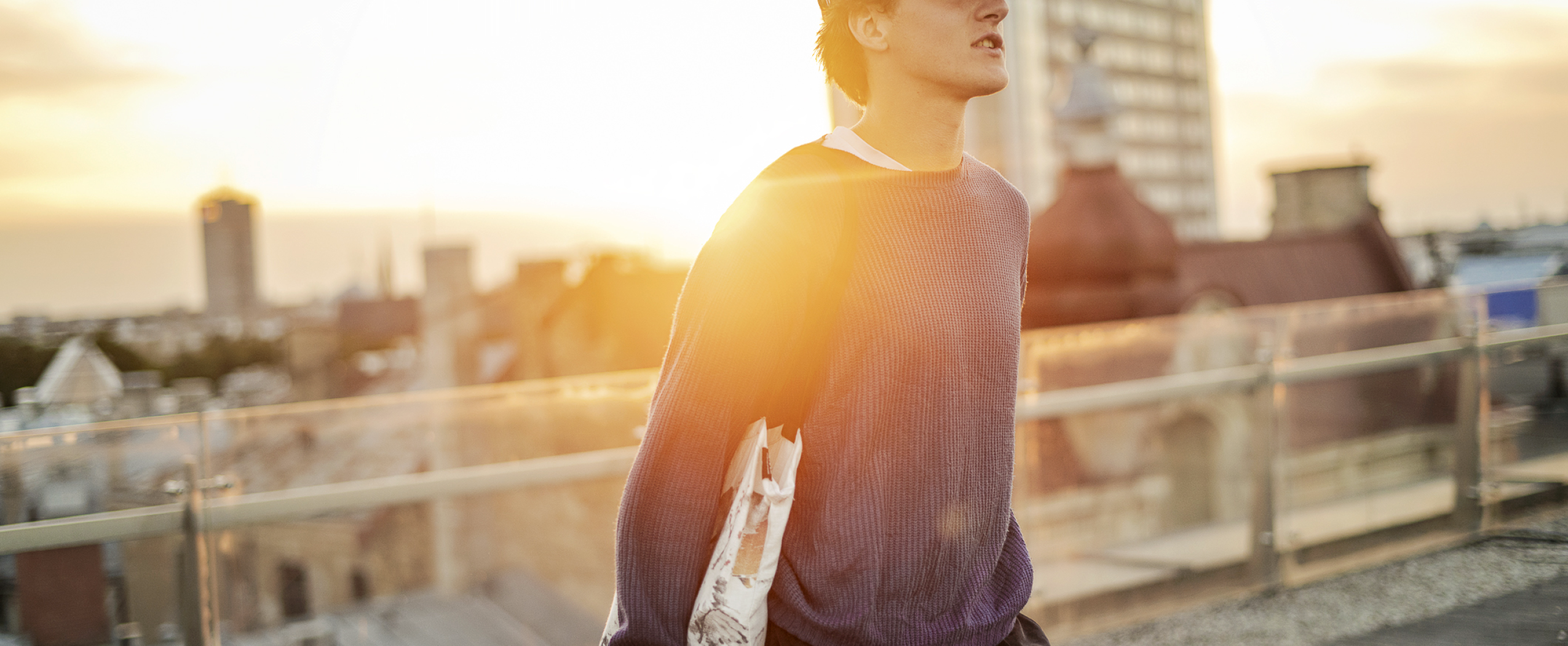 A young man stands on the rooftop of the CENTRUS building, overlooking Riga’s city skyline with towers and rooftops.